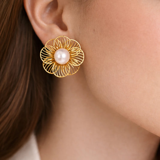 Gold floral earring with a pearl center worn by a person.