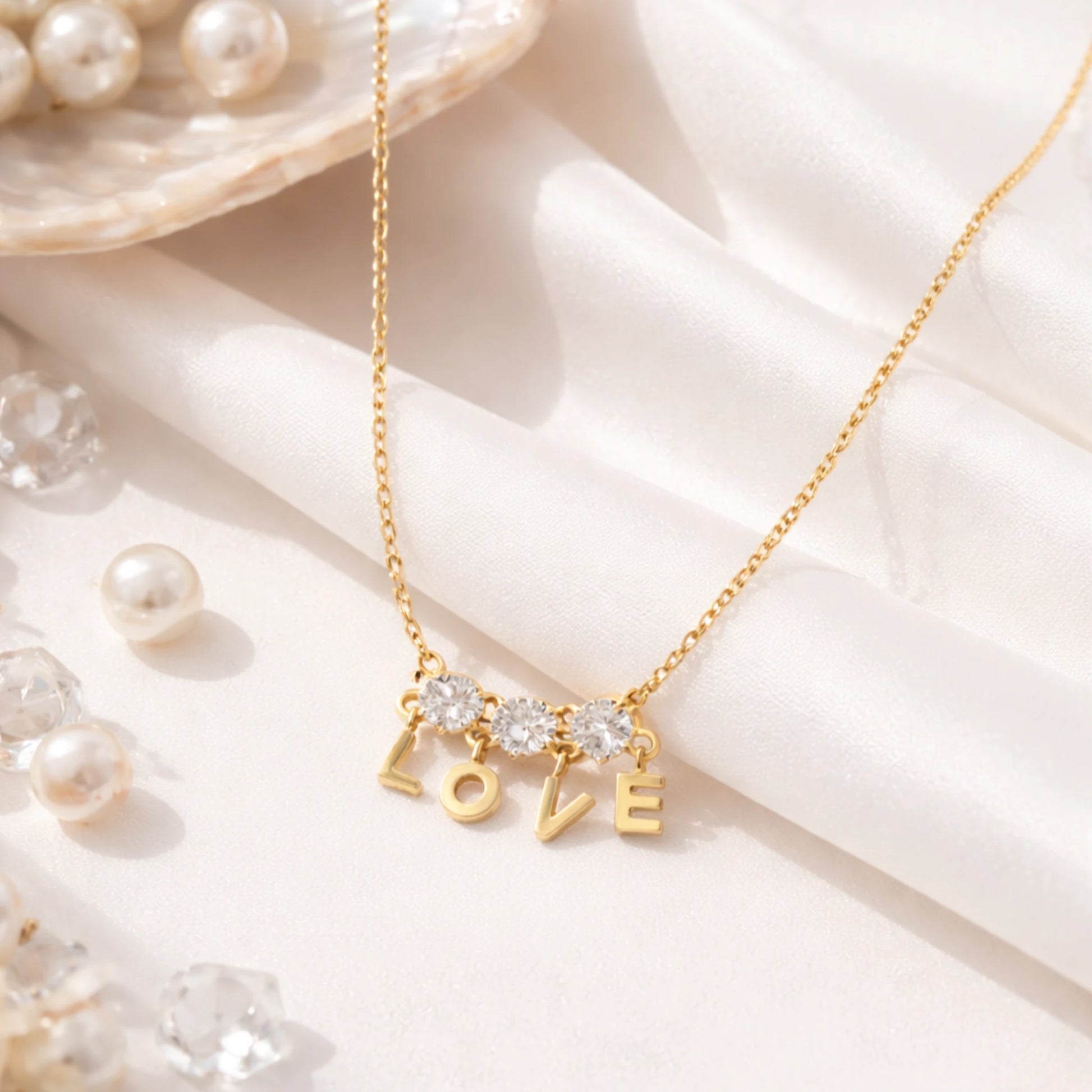 Anti tarnish gold LOVE charm necklace with cubic zirconia stones displayed on white fabric with pearl styling