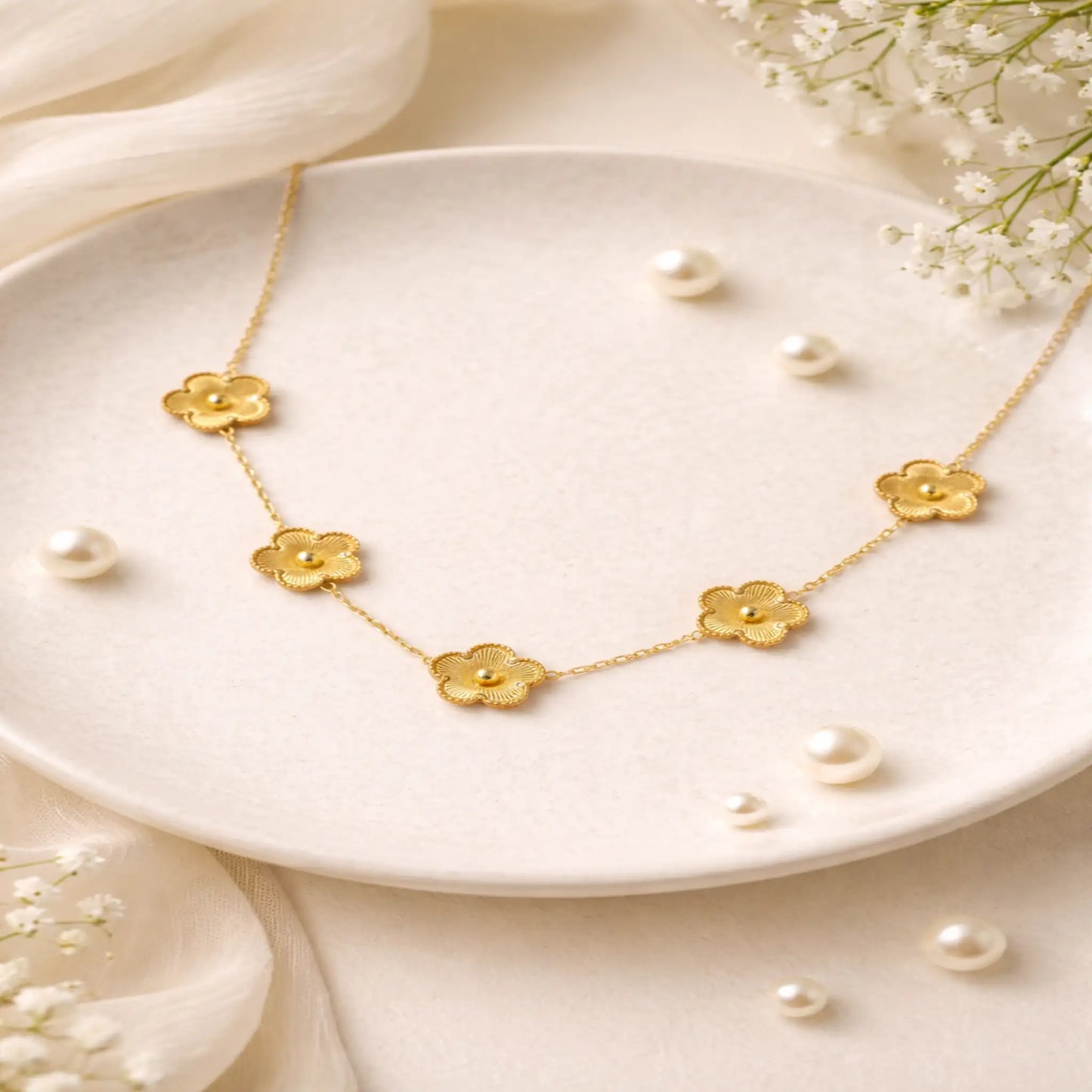 Gold necklace with floral designs on a white plate with pearls and flowers.