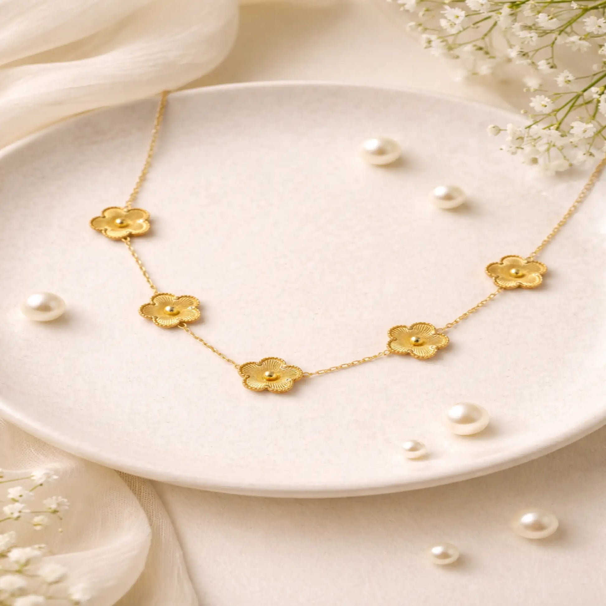Gold necklace with floral designs on a white plate with pearls and flowers.