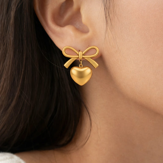 Gold bow and heart earring worn by a person with dark hair.