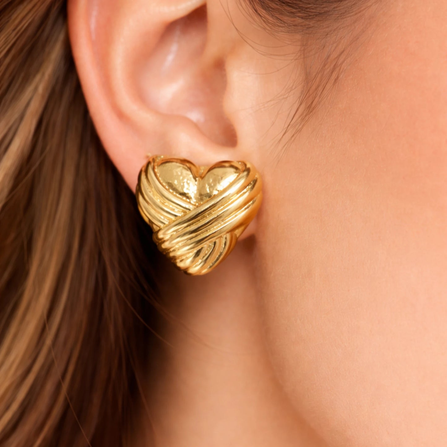 Gold heart-shaped earring worn by a person with brown hair.