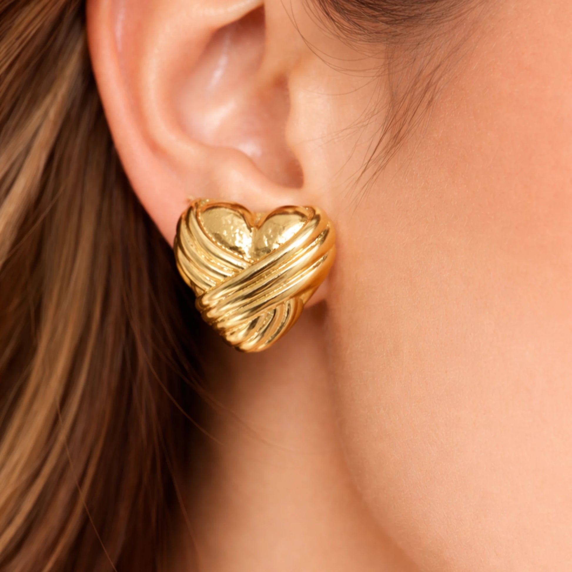 Gold heart-shaped earring worn by a person with brown hair.