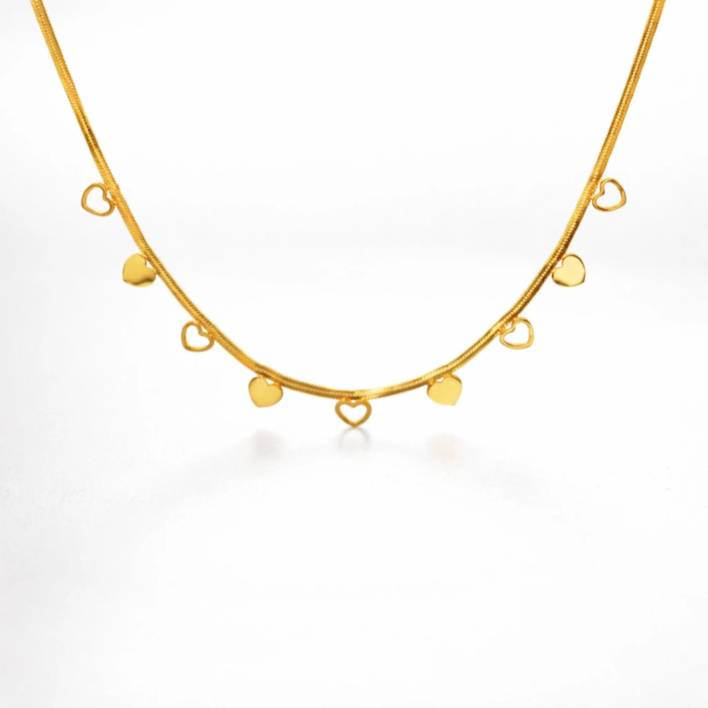 Gold necklace with open heart and closed heart pendants on a white background
