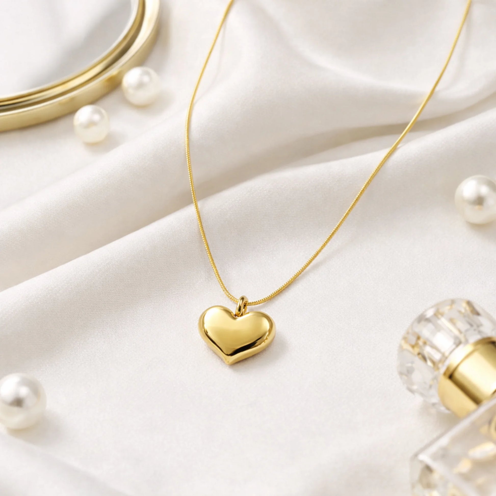 Gold heart-shaped pendant necklace on a white surface with pearls and a perfume bottle.