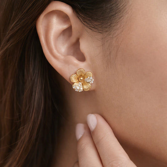 Gold floral earring with clear stones worn by a person