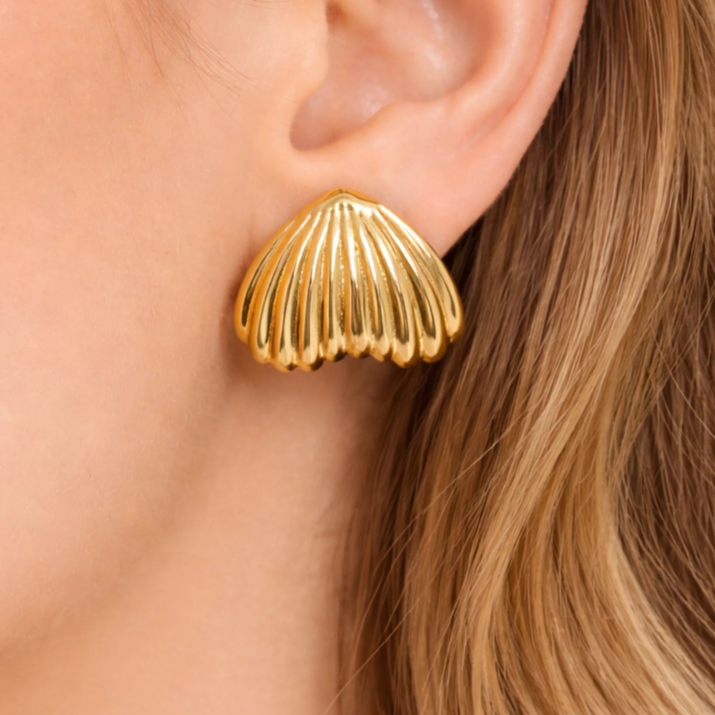 Gold shell-shaped earring worn by a person with blonde hair.