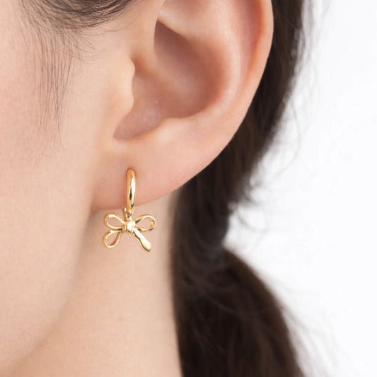 Gold bow-shaped earring worn on an ear with a blurred background