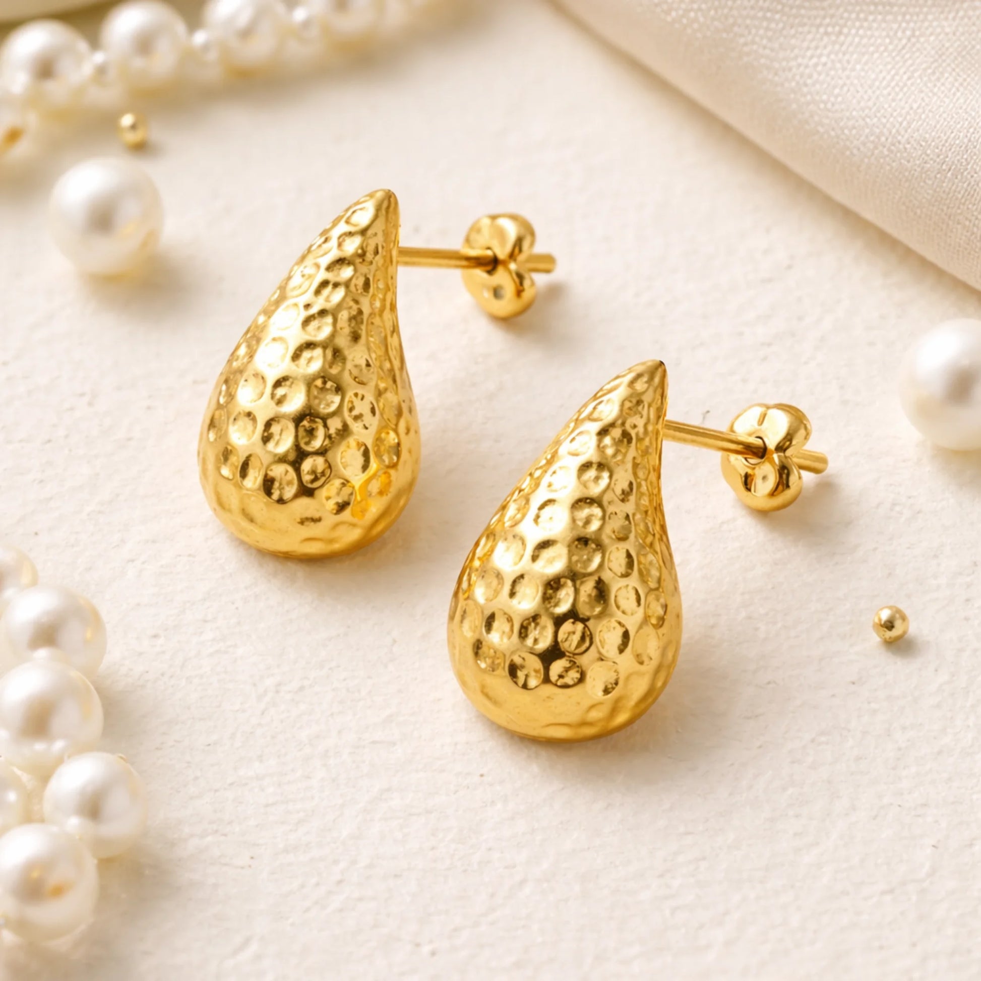 Gold teardrop earrings on a light background with pearls