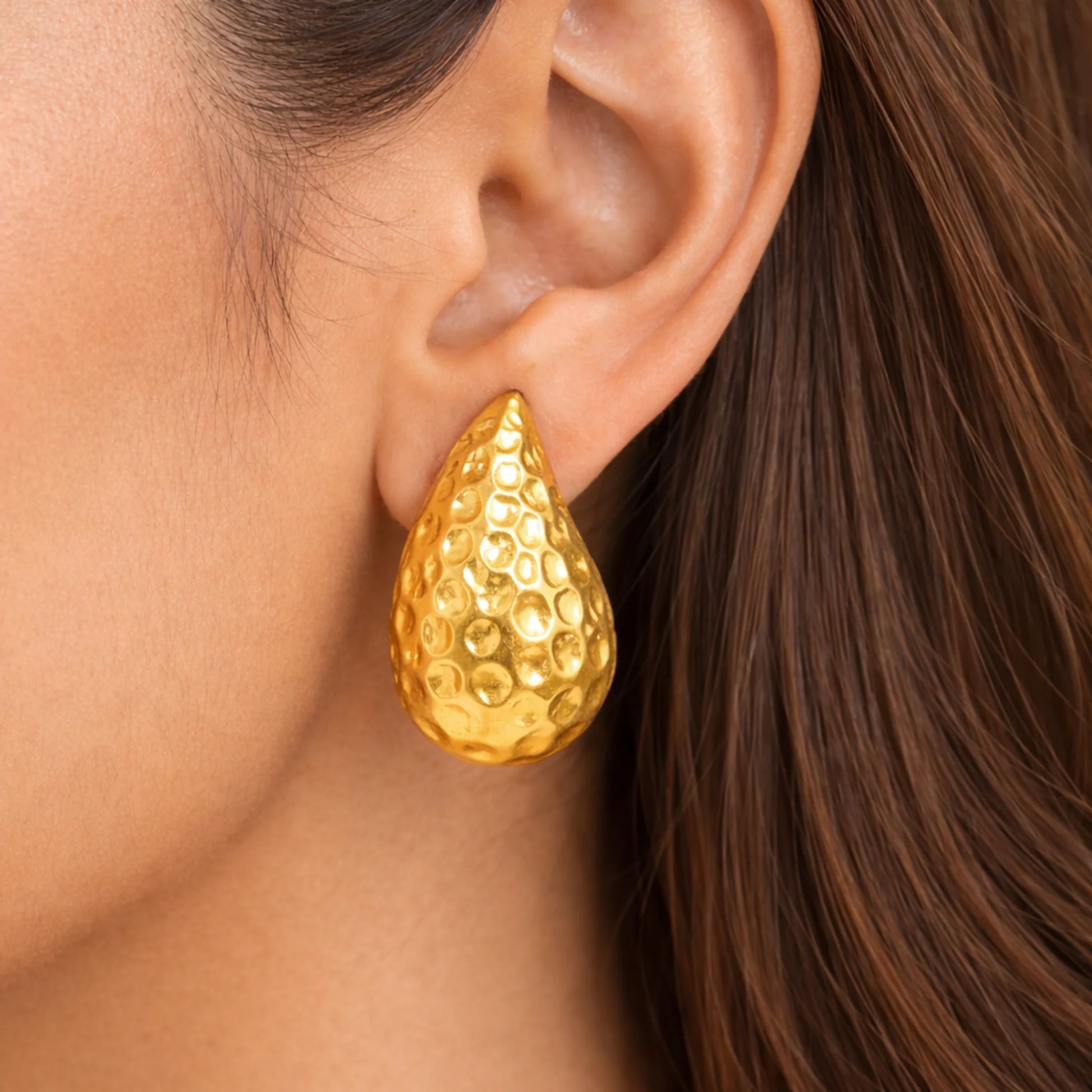 Gold teardrop earring worn by a person with brown hair.