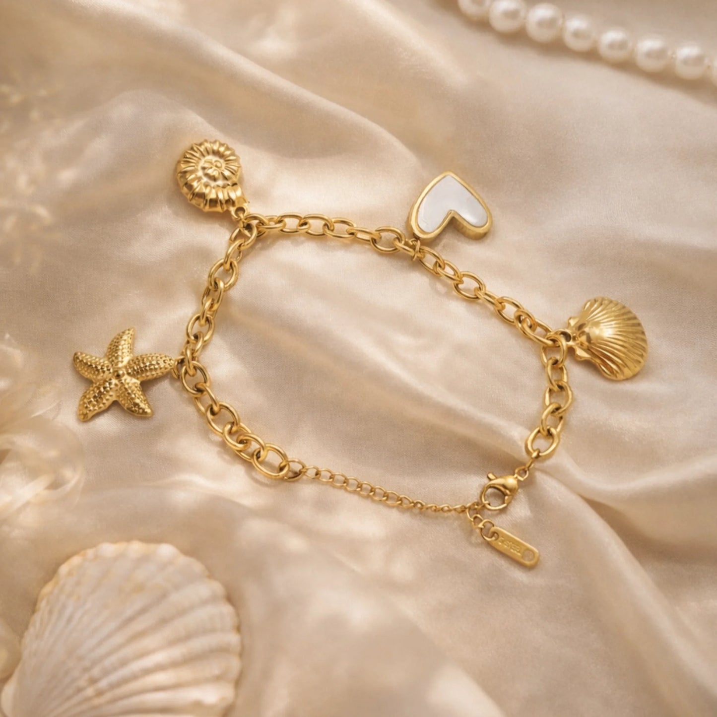 Gold bracelet with starfish, heart, and shell charms on a beige fabric background