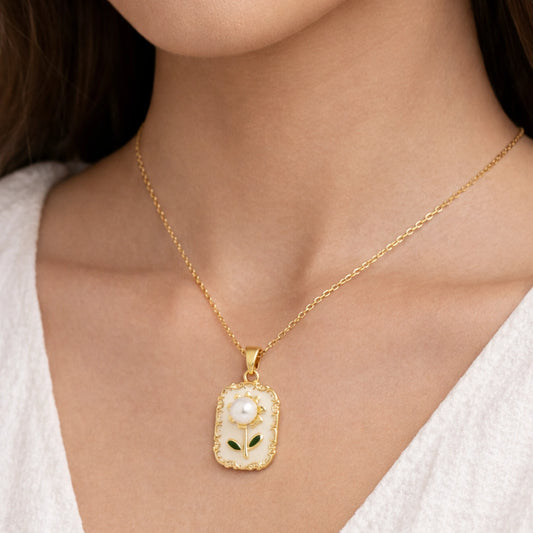 Gold necklace with a pendant featuring a pearl and green leaves on a person wearing a white top.