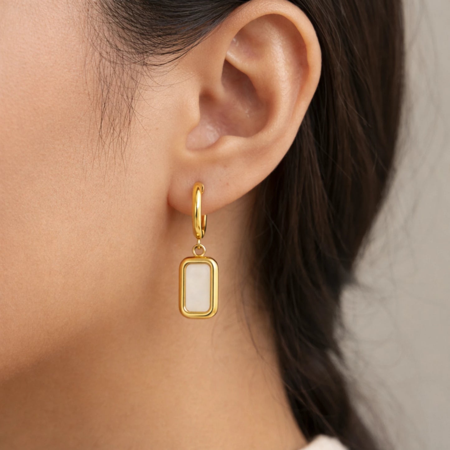 Gold earring with a white stone worn by a person