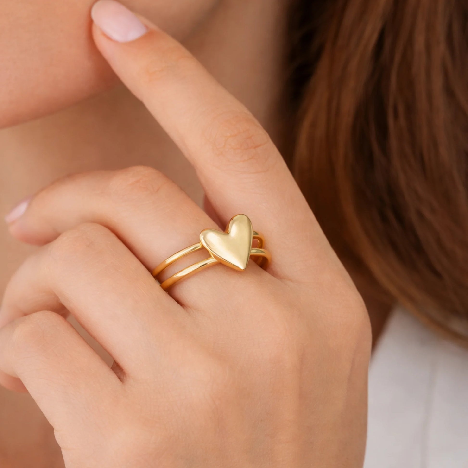 Gold heart-shaped ring on a finger with a blurred background