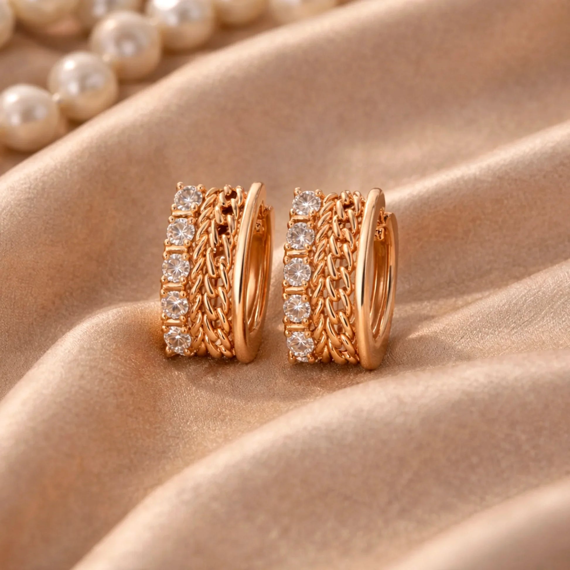 YUBIRAA gold huggie hoop earrings with diamond row and chain texture, side angle on satin background
