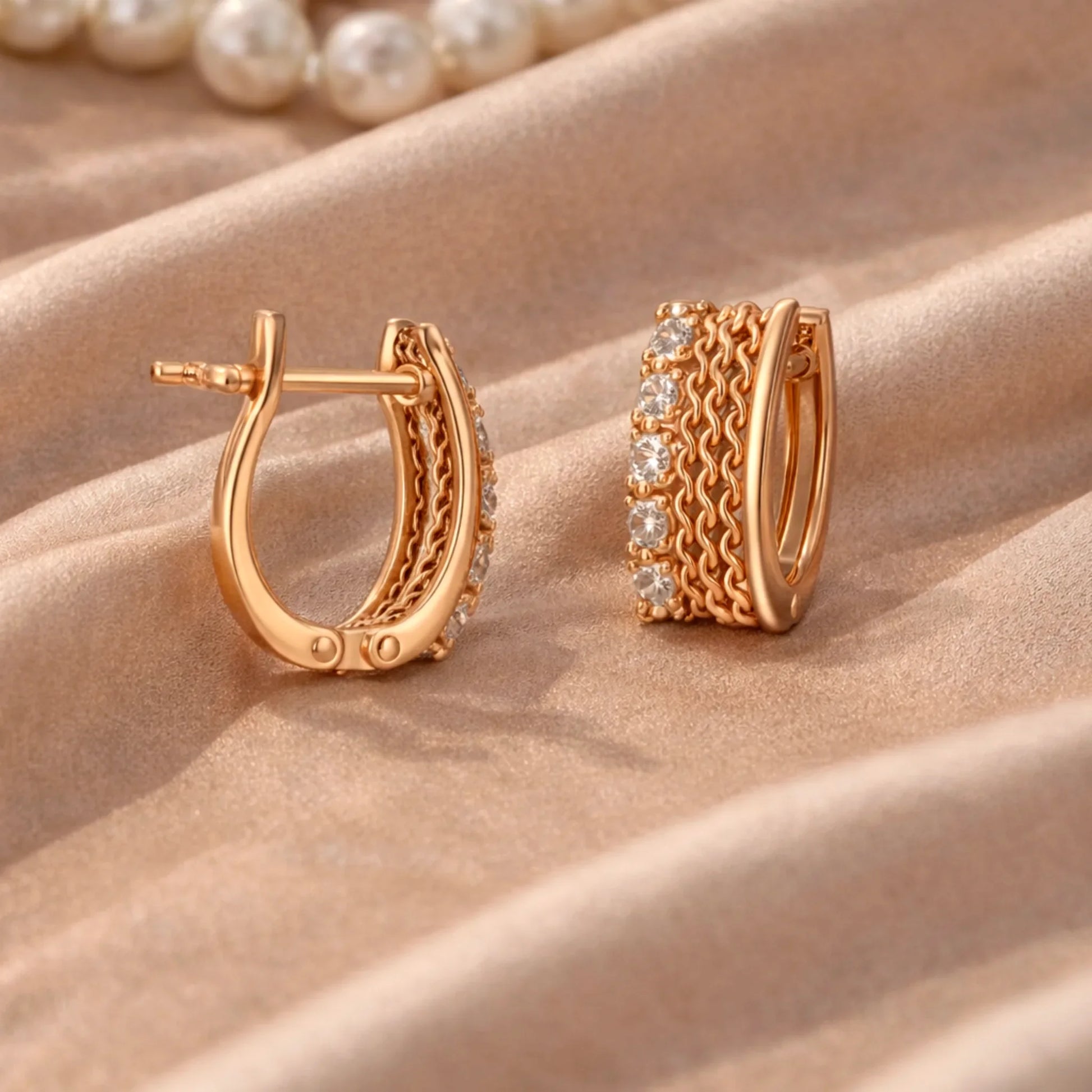 YUBIRAA gold huggie hoop earrings with chain design and diamonds placed on satin fabric with pearls