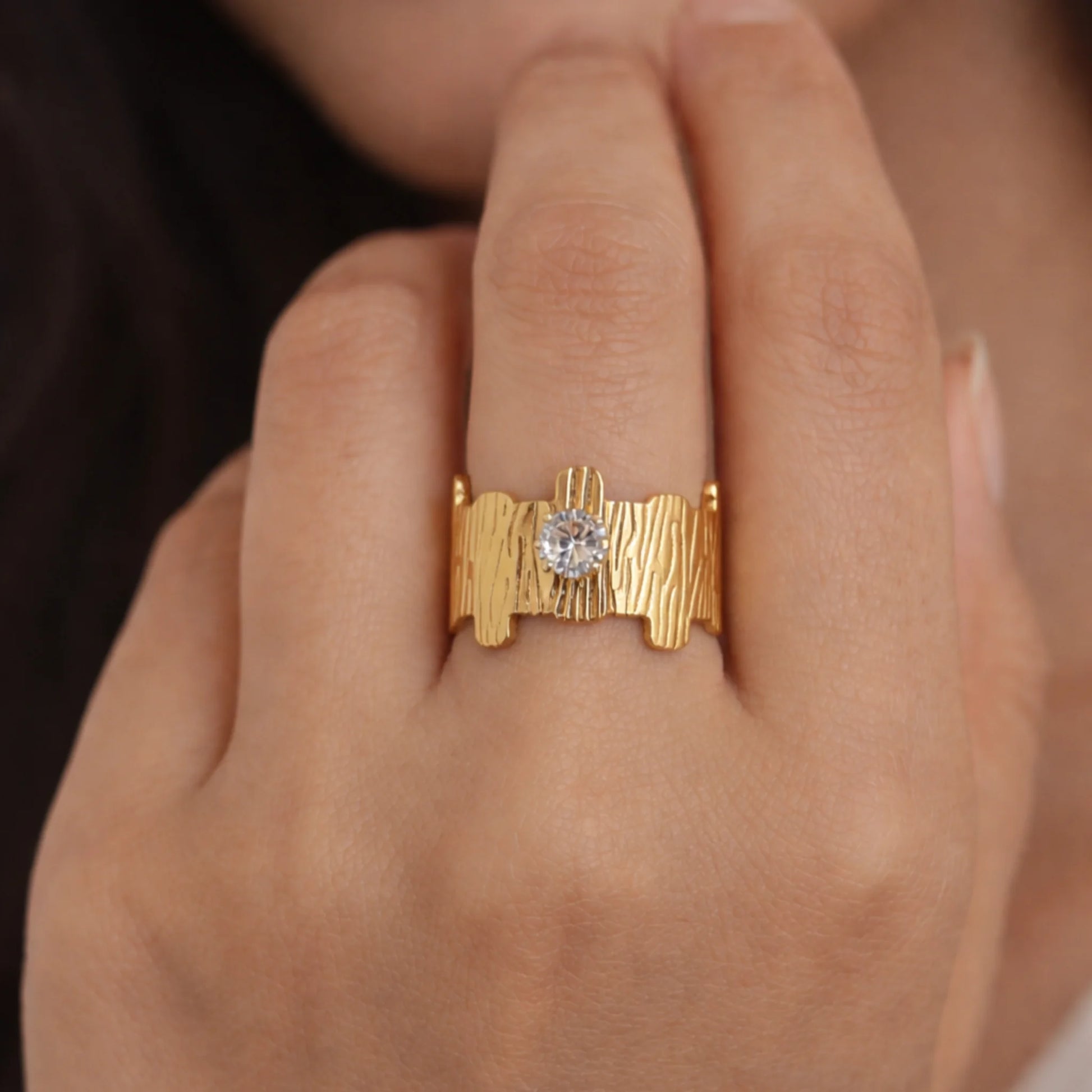 Woman wearing a gold plated ring with a textured organic band and round solitaire stone, shown in a close-up hand view