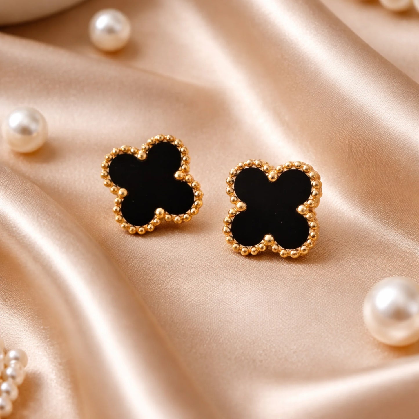Black clover-shaped earrings with gold borders on a satin surface