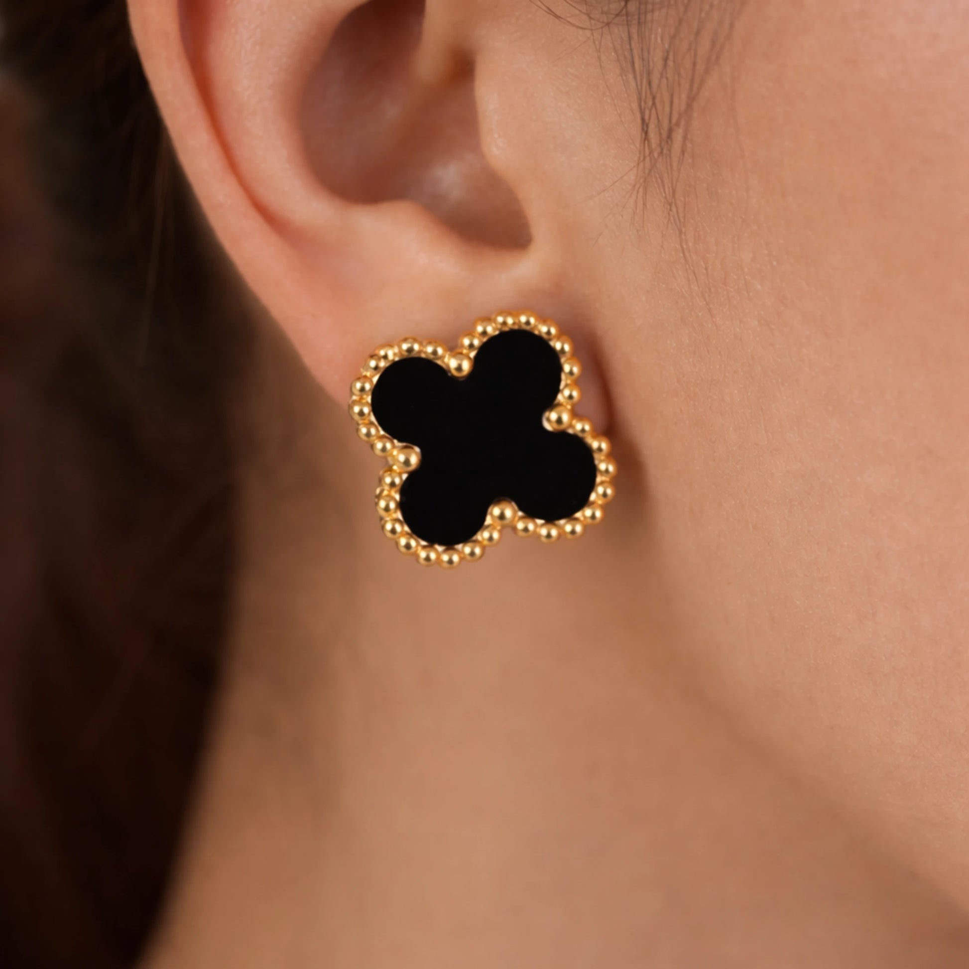 Black clover-shaped earring with gold accents on an ear