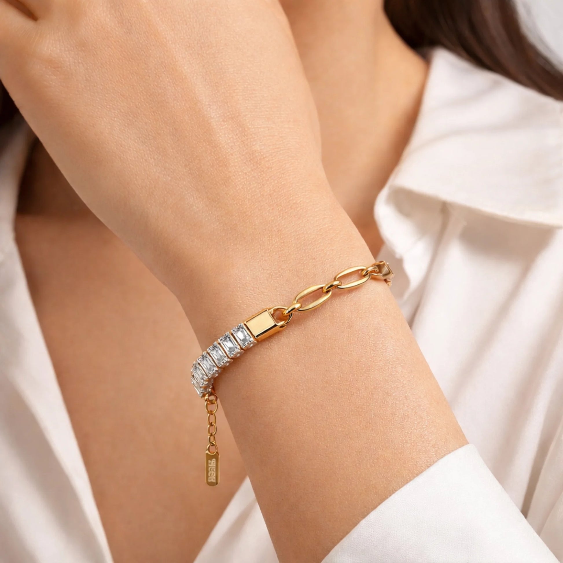 Gold bracelet with diamonds on a person's wrist, wearing a white shirt.