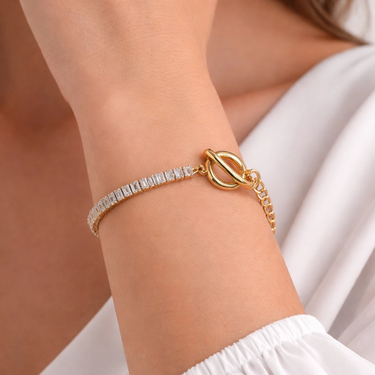 Gold bracelet with a white stone on a wrist against a neutral background