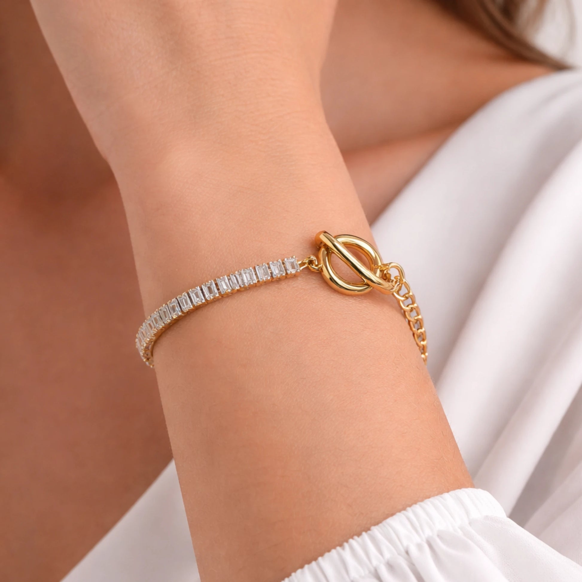 Gold bracelet with a white stone on a wrist against a neutral background