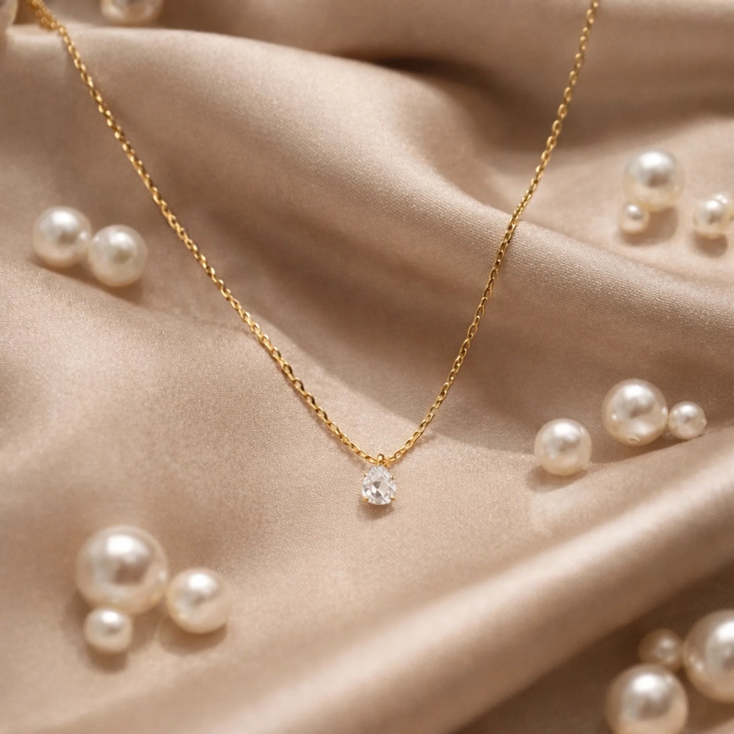 Gold necklace with a diamond pendant on a beige fabric background with scattered pearls.