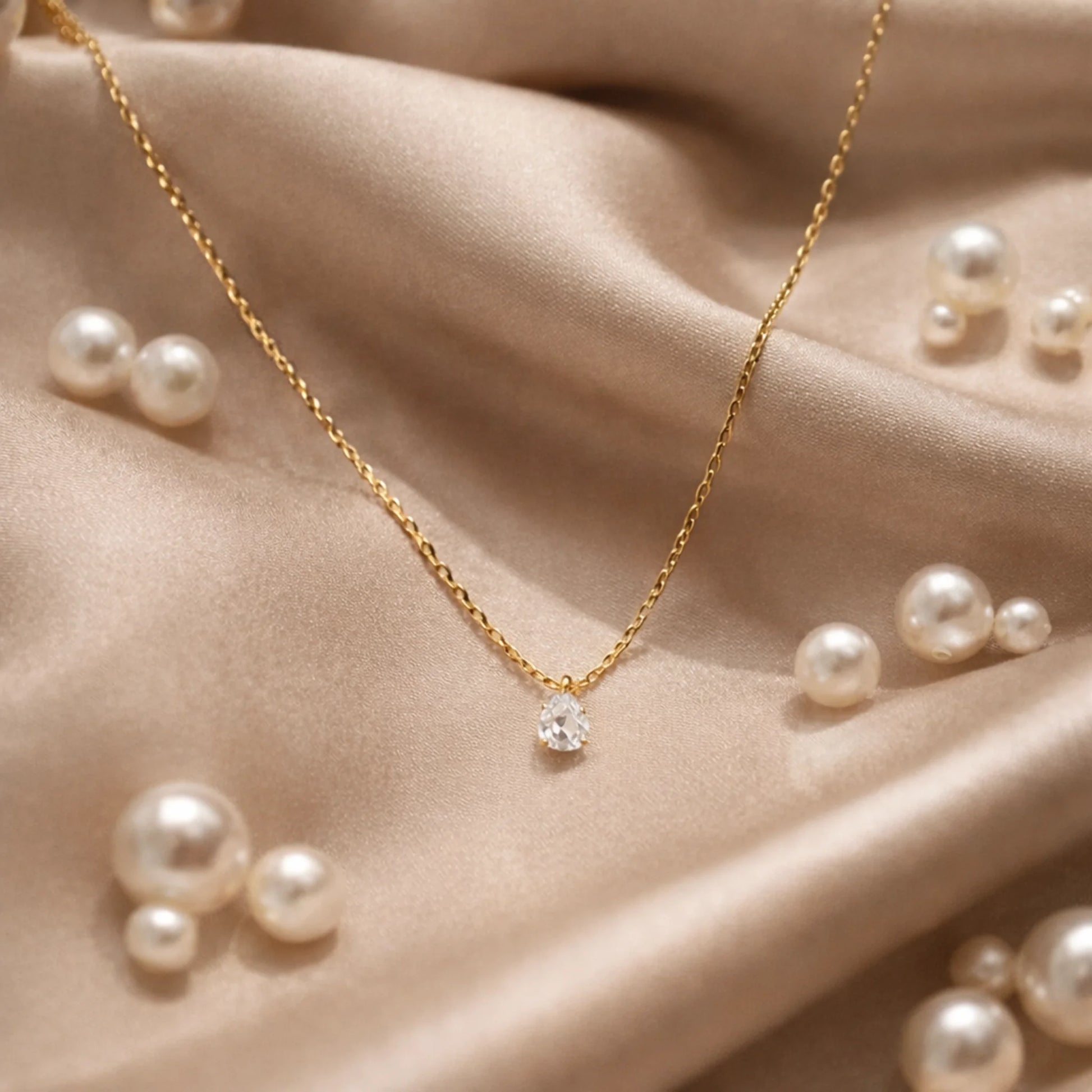 Gold necklace with a diamond pendant on a beige fabric background with scattered pearls.