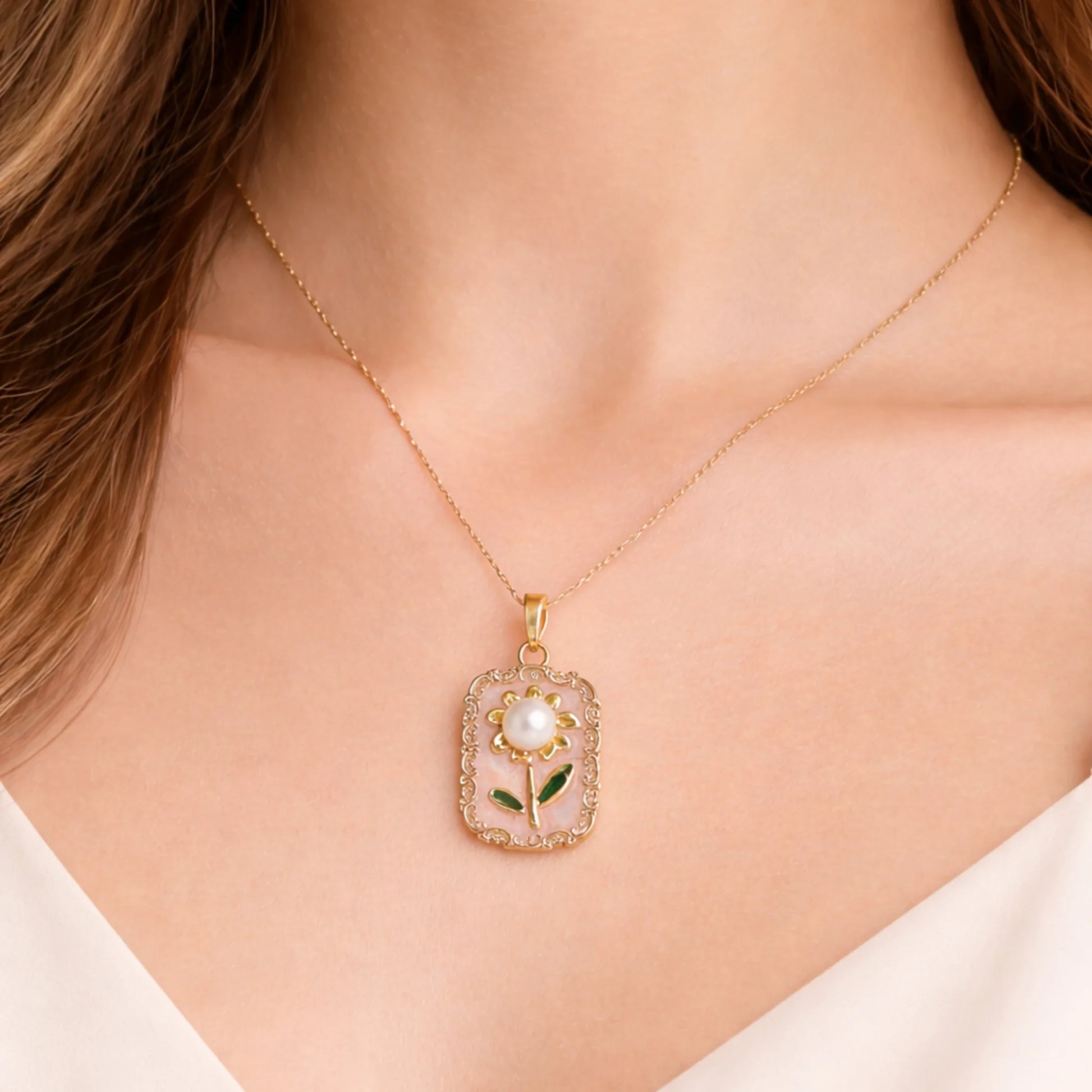 Gold necklace with a floral pendant on a person wearing a white top