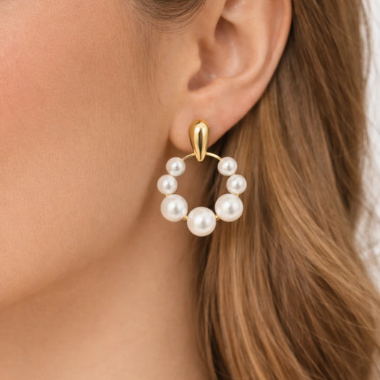 Gold earring with pearl-like beads worn by a person with brown hair.