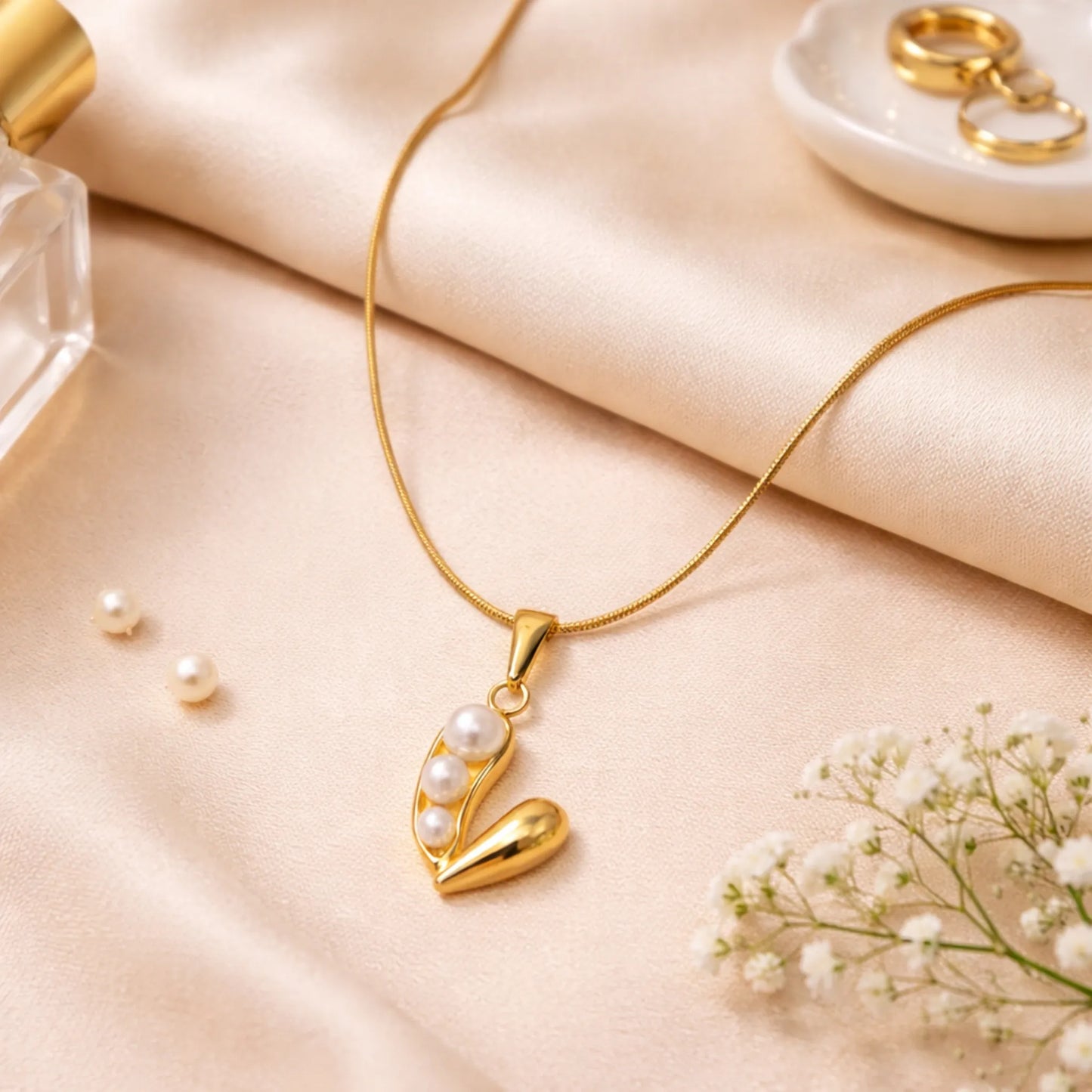 Gold necklace with a v-shaped pendant on a soft beige surface with flowers.