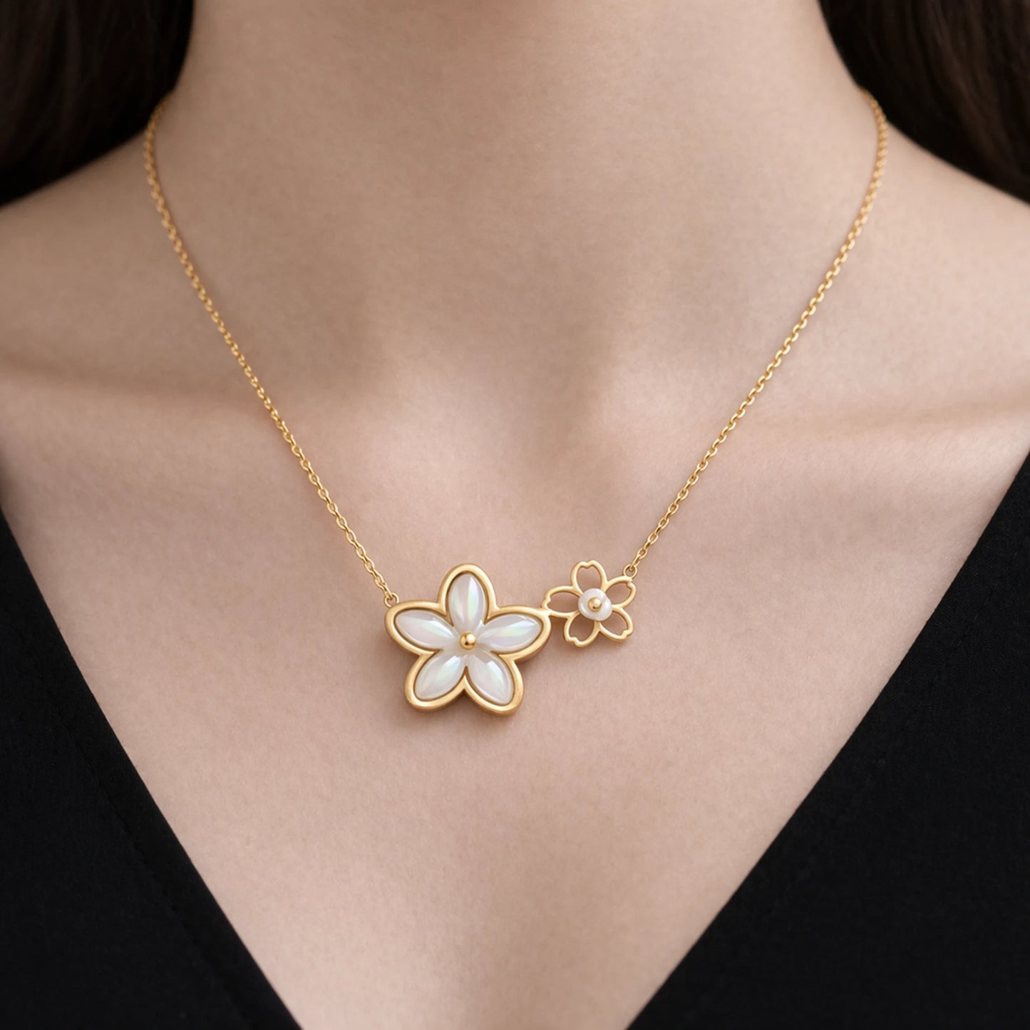 Gold necklace with a floral pendant on a person wearing a black top