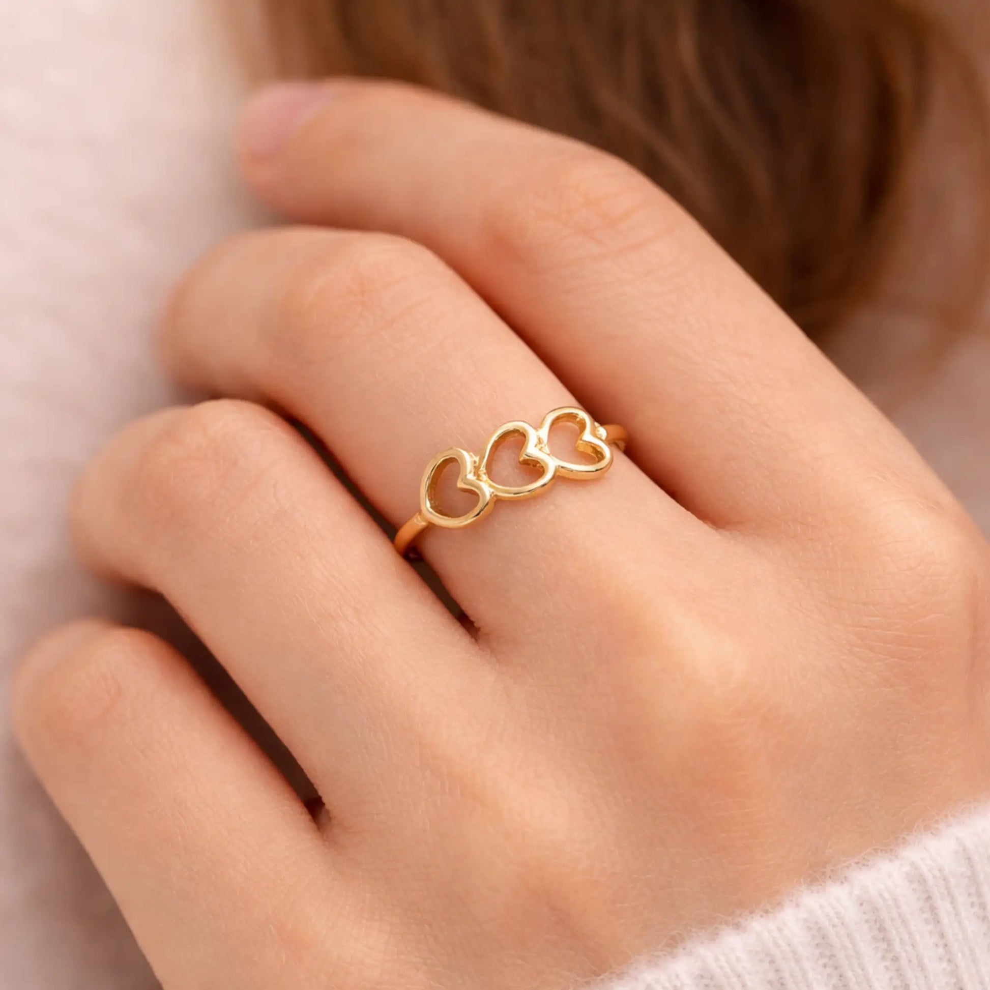 YUBIRAA triple heart gold ring worn on finger, showcasing delicate open-heart design and adjustable fit
