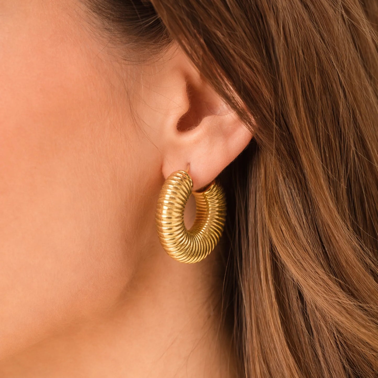 Gold hoop earring worn by a person with brown hair.