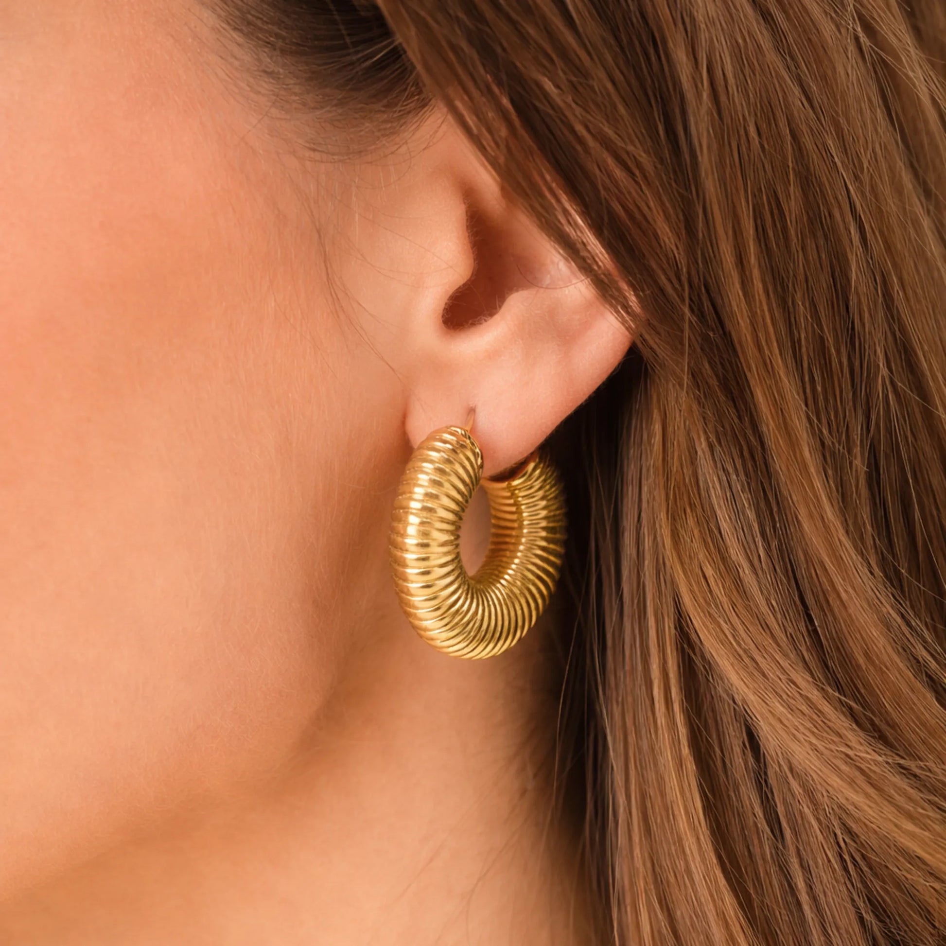 Gold hoop earring worn by a person with brown hair.