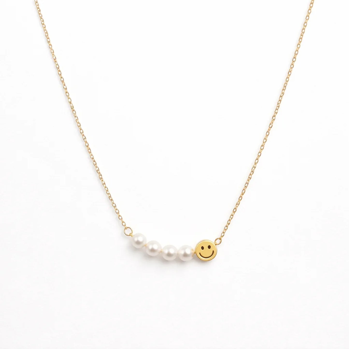 Gold necklace with a pearl and smiley face charm on a white background