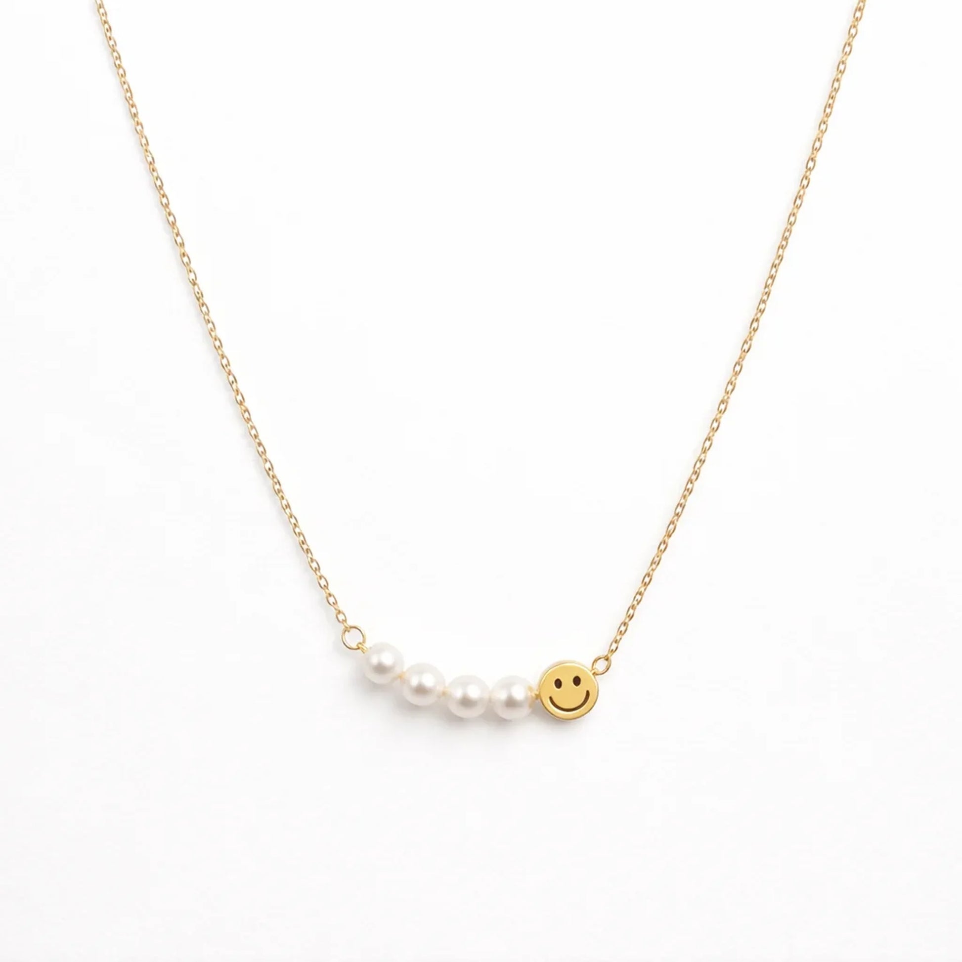 Gold necklace with a pearl and smiley face charm on a white background