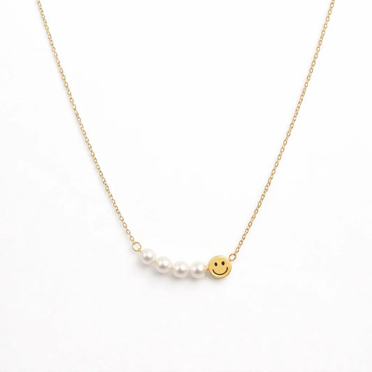 Gold necklace with a pearl and smiley face charm on a white background