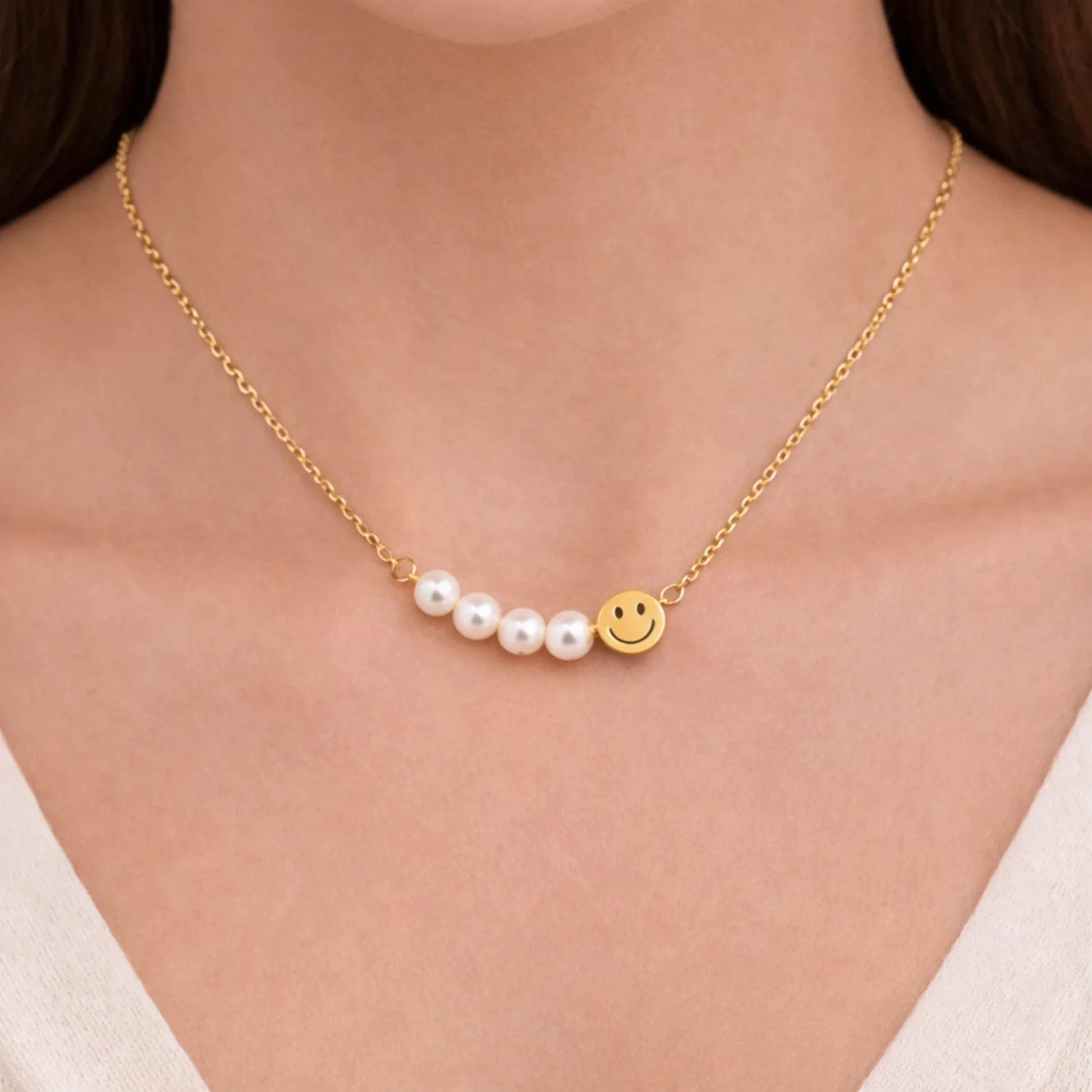 Gold necklace with pearls and a smiley face charm on a person wearing a white top.