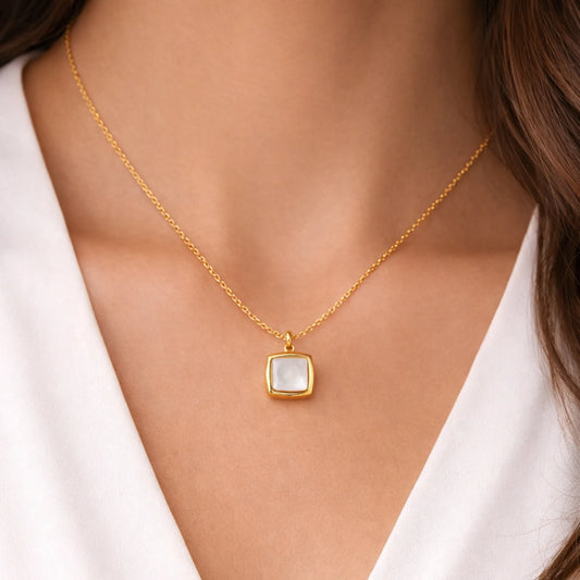 Gold necklace with a square pendant worn by a person against a white background