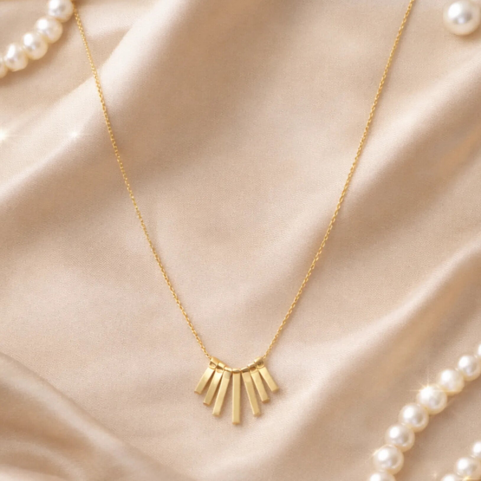Elegant gold bar pendant anti tarnish necklace styled on satin fabric with pearls