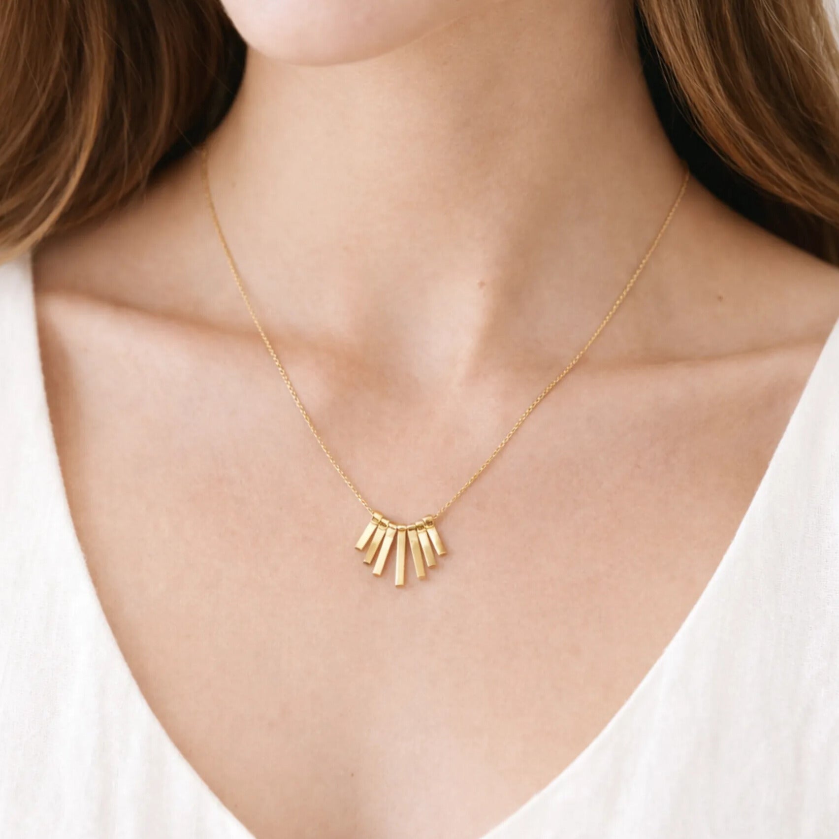 Gold necklace with a geometric pendant on a person wearing a white top.