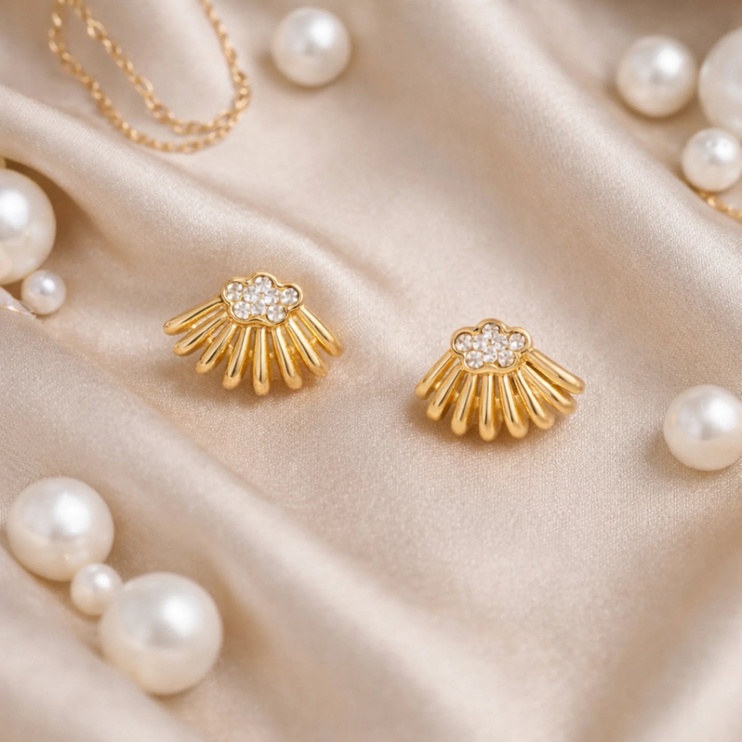 Gold shell-shaped stud earrings placed on satin fabric with pearls