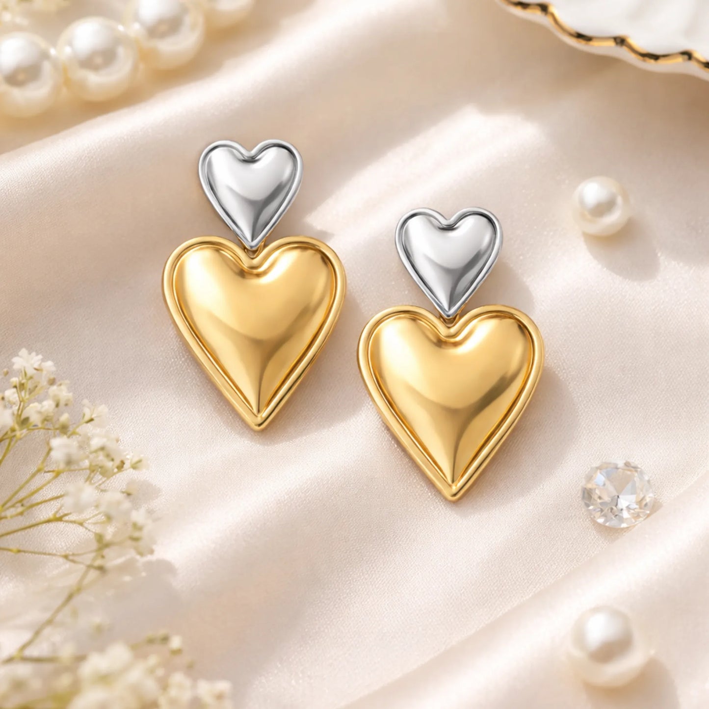 Heart-shaped earrings in gold and silver on a soft beige background with pearls and flowers.