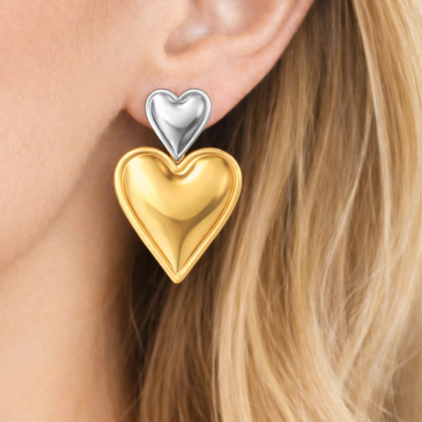 Gold and silver heart-shaped earrings worn by a person with blonde hair.