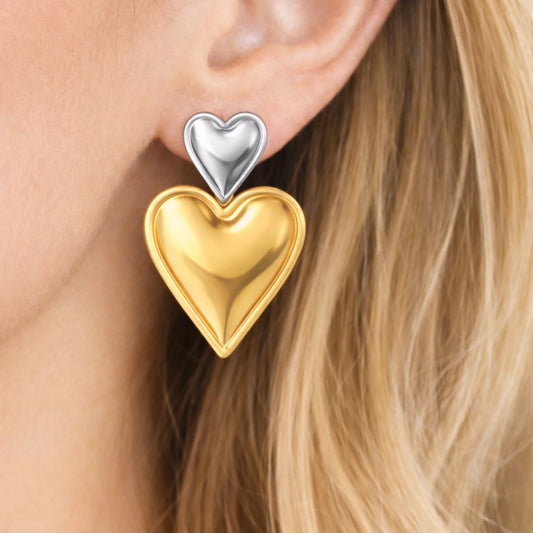 Gold and silver heart-shaped earrings worn by a person with blonde hair.