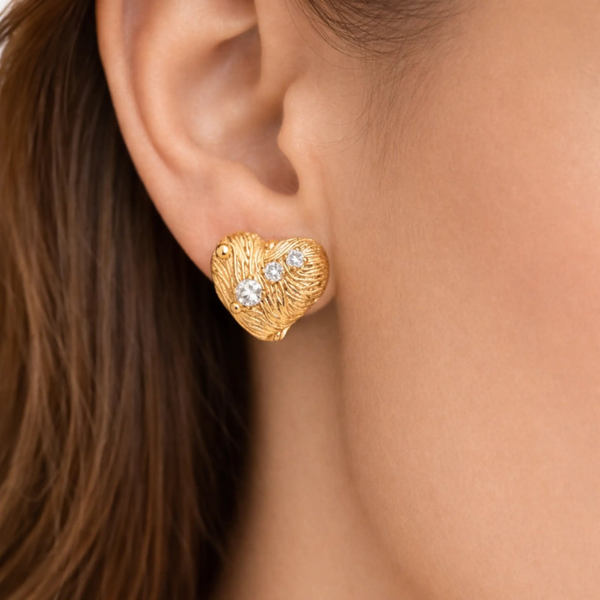 Model wearing anti-tarnish gold plated heart-shaped stud earrings with textured finish and cubic zirconia stones