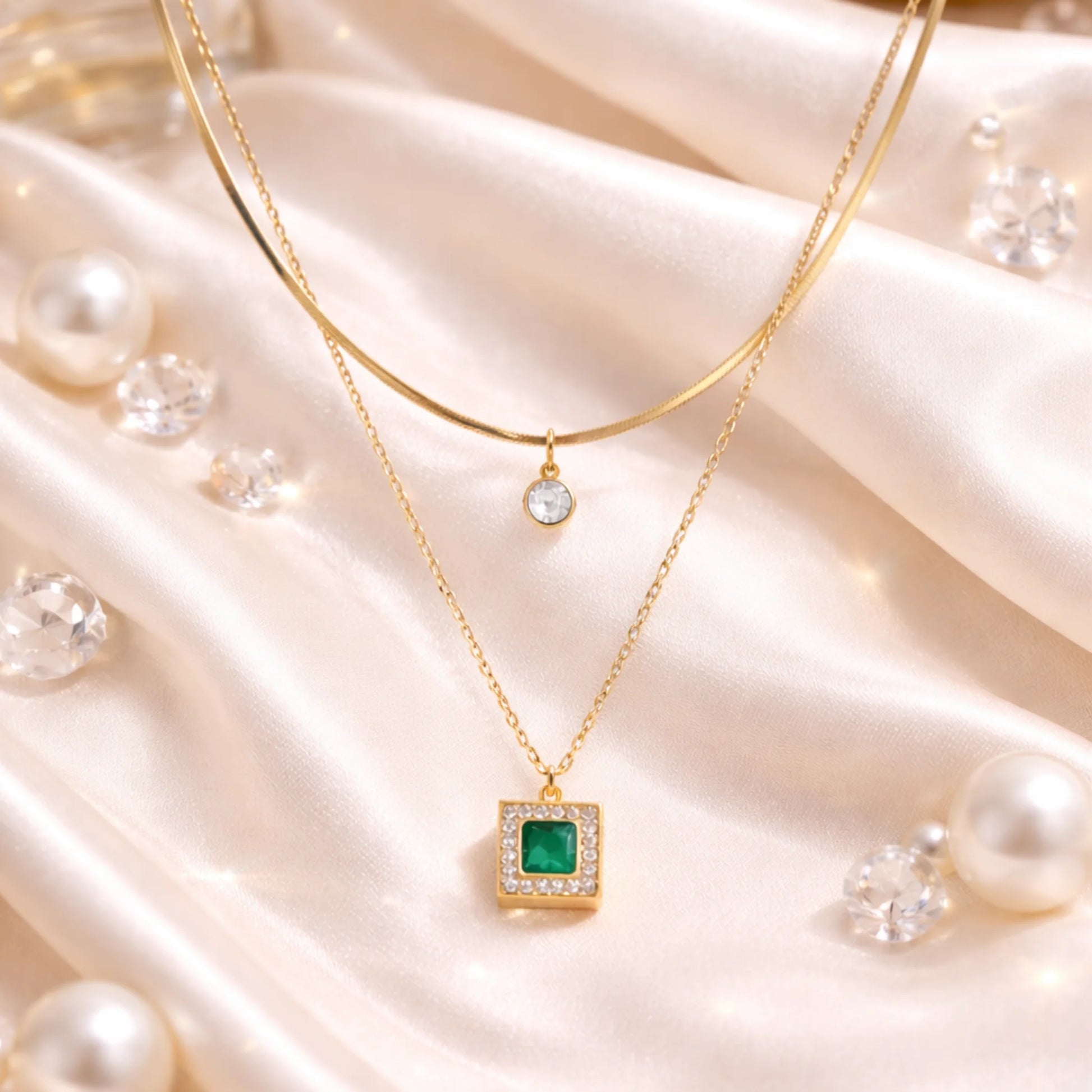 Gold layered necklace with green stone pendant styled on satin fabric with pearls for elegant everyday jewellery look