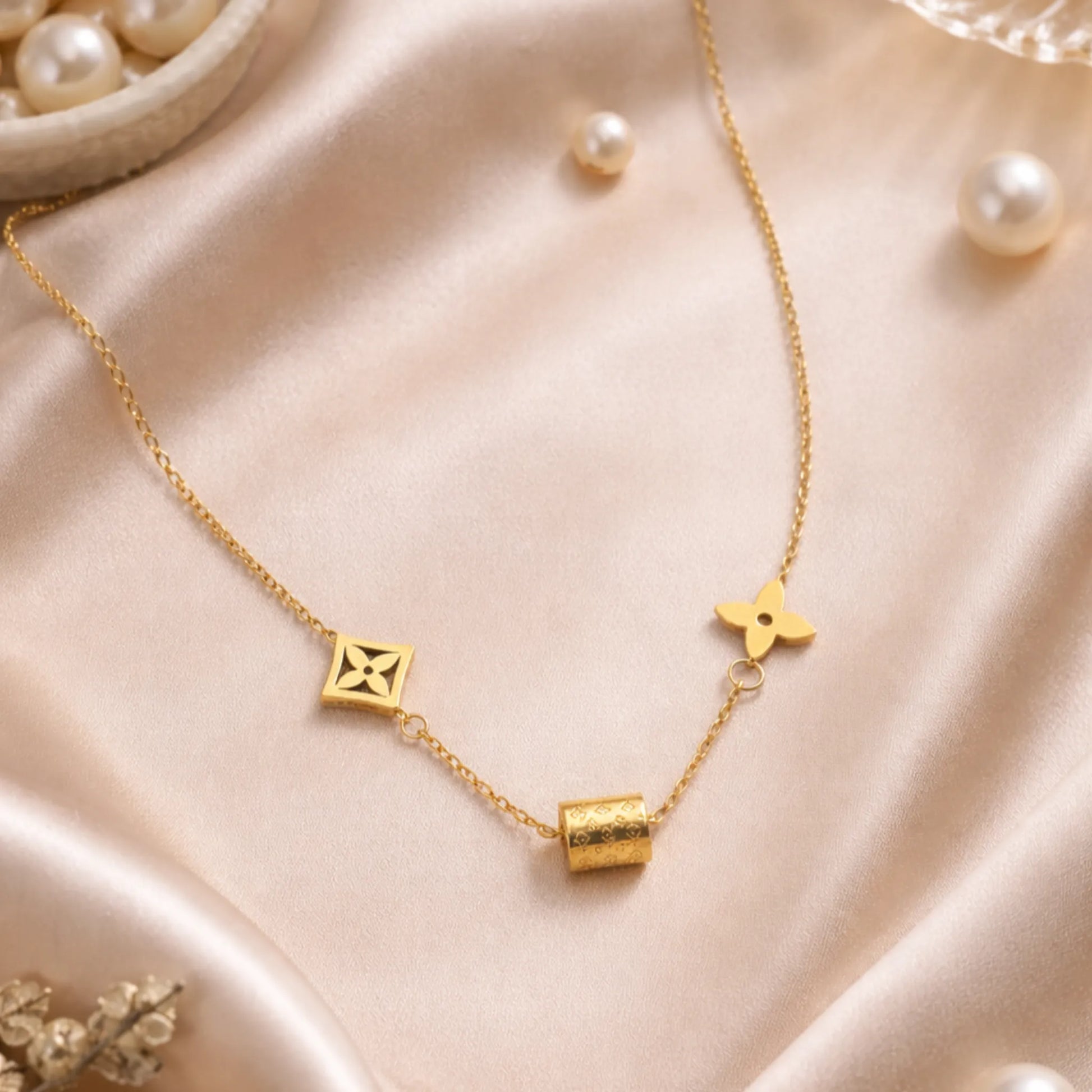 Gold charm necklace styled on champagne satin fabric with pearls in soft aesthetic flat lay
