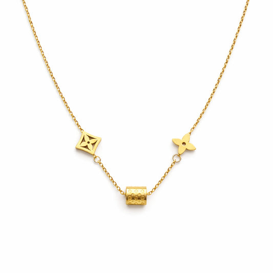 Gold charm necklace with geometric motifs and engraved cylindrical bead on white background